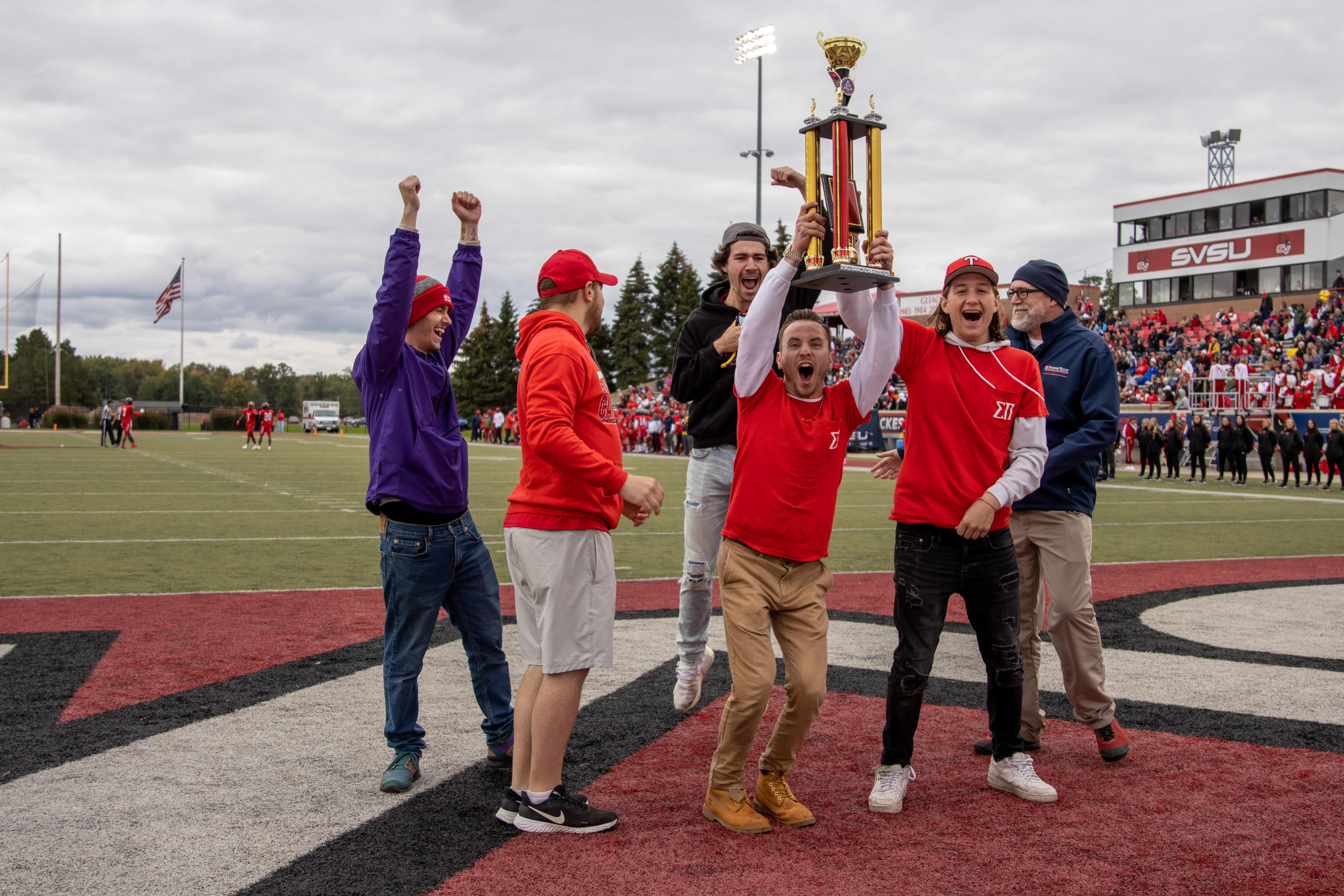 Students cheering at the end zone holding the trophy for winning the Homecoming RSO competition.